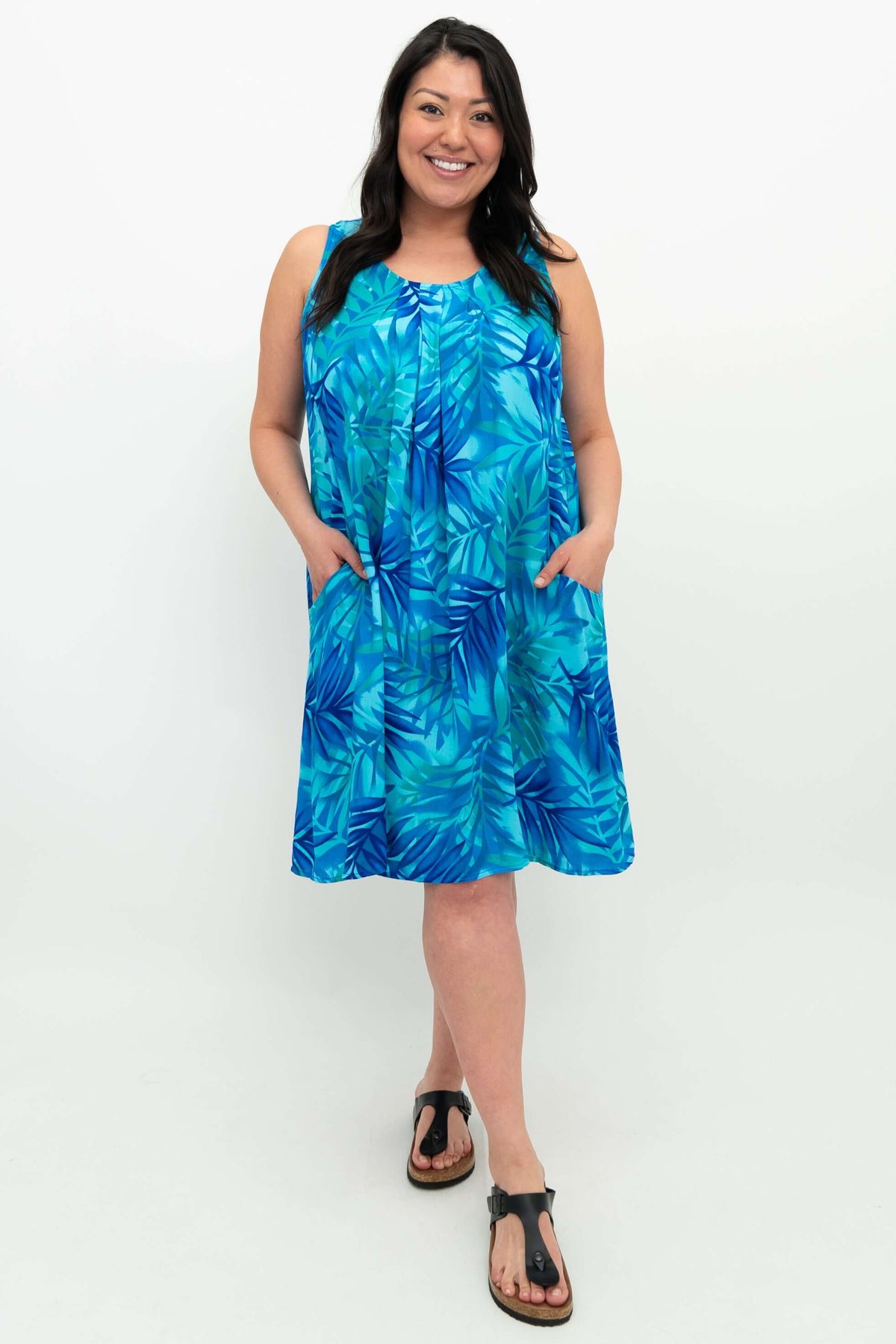 Woman wearing a sleeveless blue leaf print dress with pockets, front view