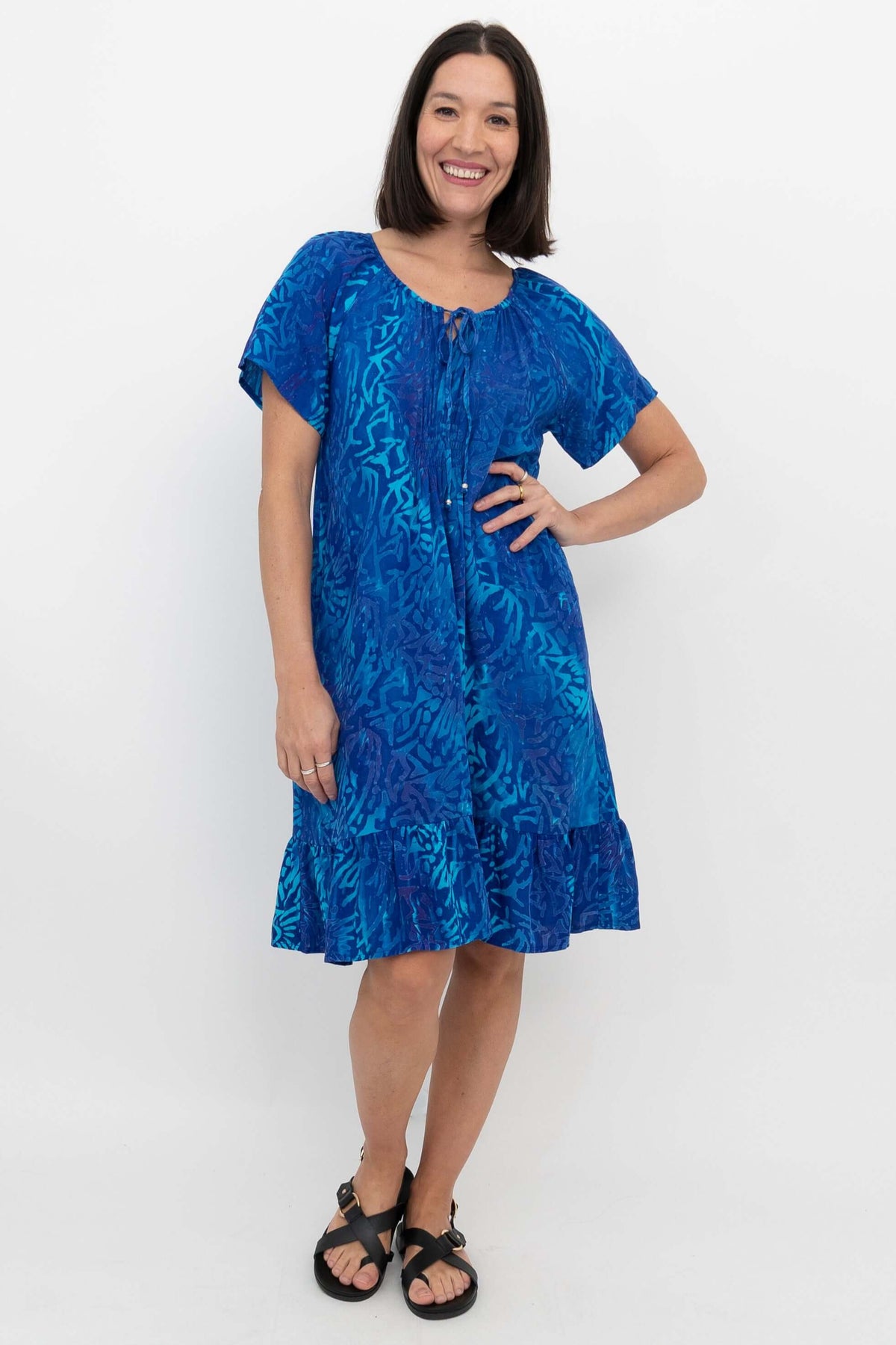 Model wearing bright blue Samoa Dress with ruffle hem and tie neckline, front view