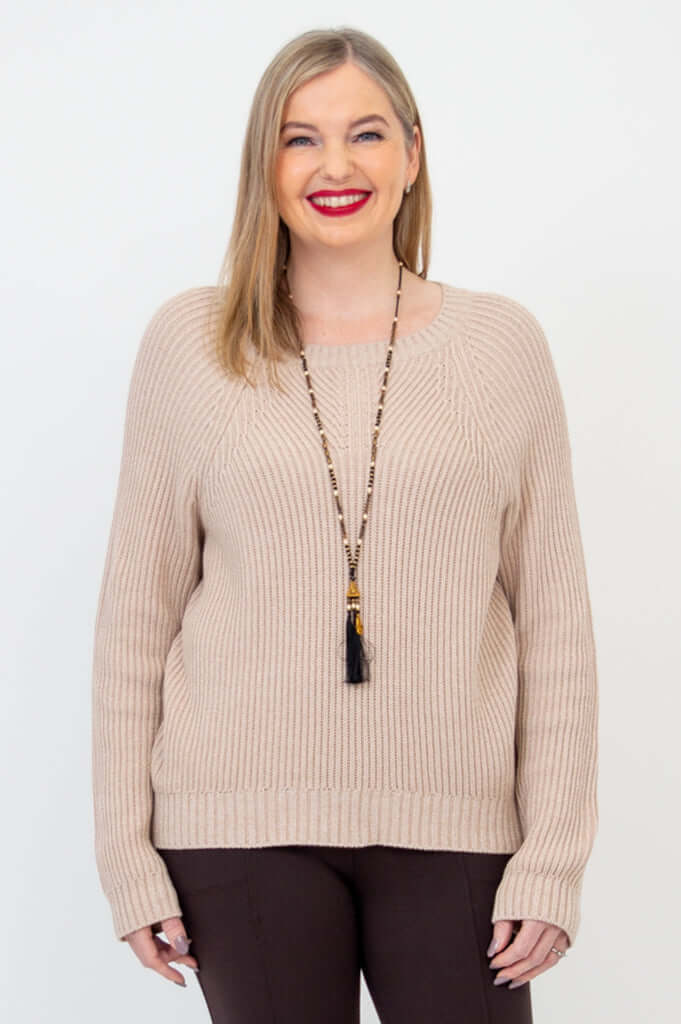 Front view of a woman wearing a beige knit Davis Sweater over brown pants