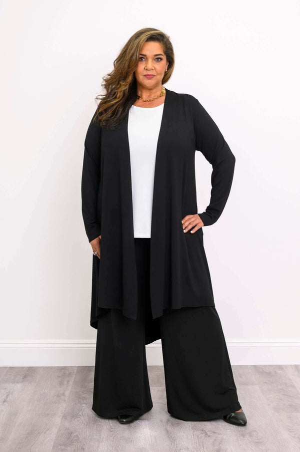 Front view of model wearing black high-low duster cardigan over white top and wide-leg pants