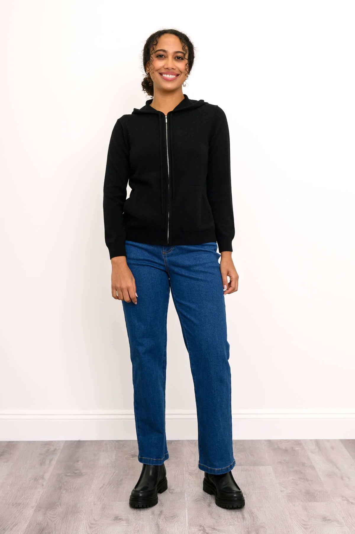 Woman standing and smiling in black hoodie and blue jeans, facing forward