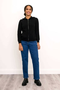 Woman standing and smiling in black hoodie and blue jeans, facing forward