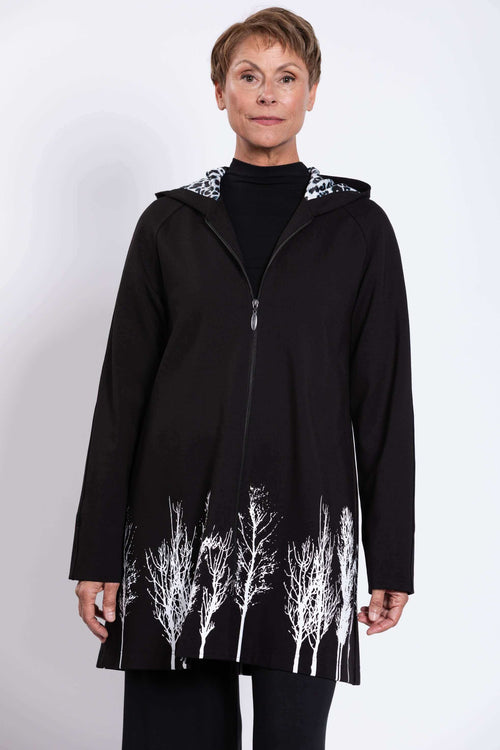 Front view of model wearing black zippered coat with white silhouetted tree border