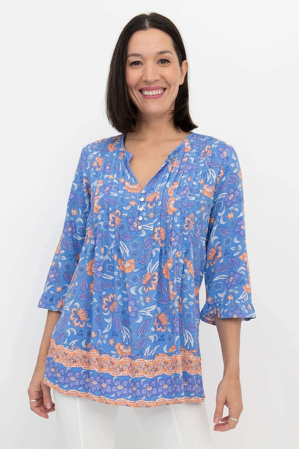 Front view of a woman wearing a blue and orange floral peasant blouse with pleated details
