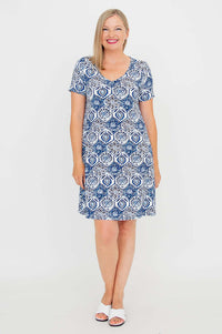 Front view of a woman in a short sleeve blue and white mosaic pattern dress, standing and smiling