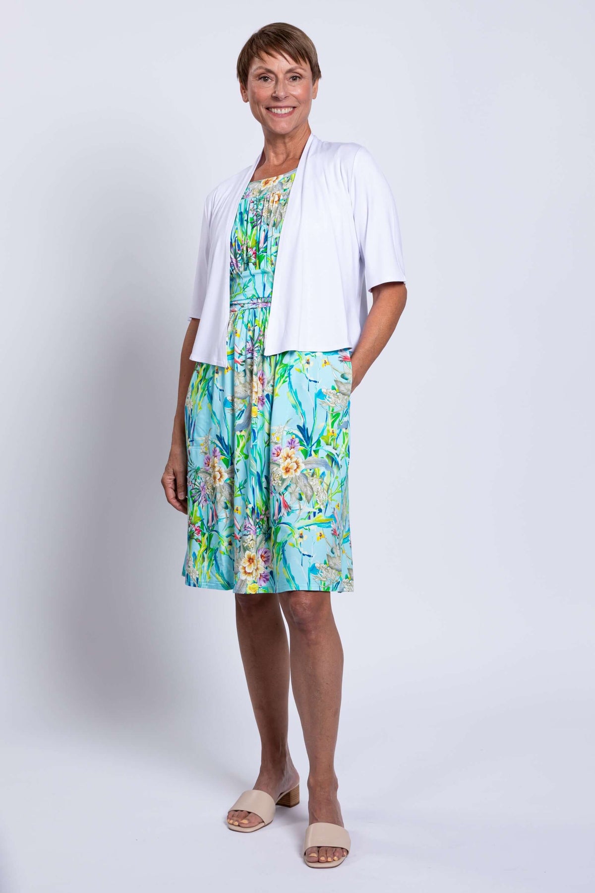 Front view of blue floral ruched dress with white cardigan and pockets