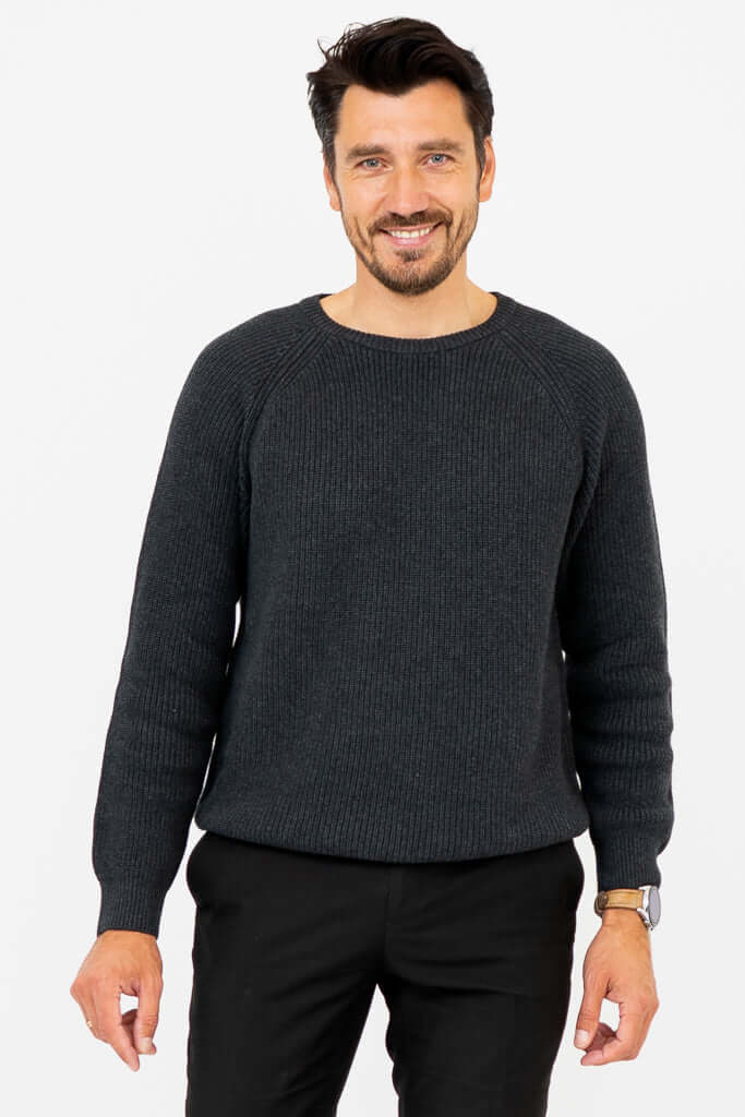 Man wearing a charcoal ribbed crewneck sweater, smiling with hands relaxed