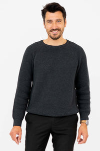 Man wearing a charcoal ribbed crewneck sweater, smiling with hands relaxed