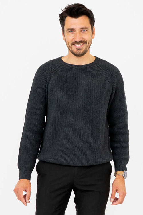 Man wearing a charcoal ribbed crewneck sweater, smiling with hands relaxed