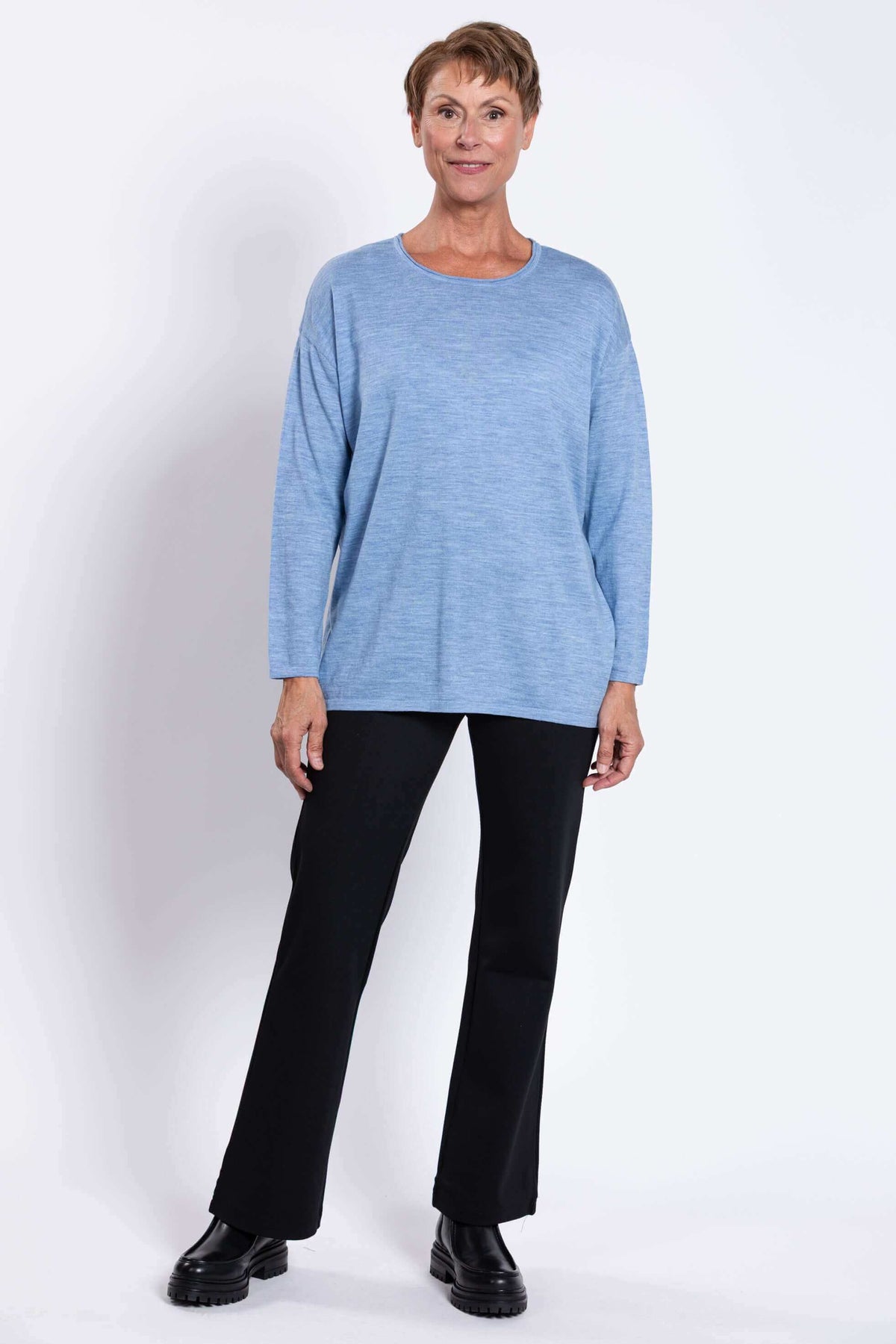 Front view of a woman in a blue merino wool pullover sweater and black pants, hands relaxed