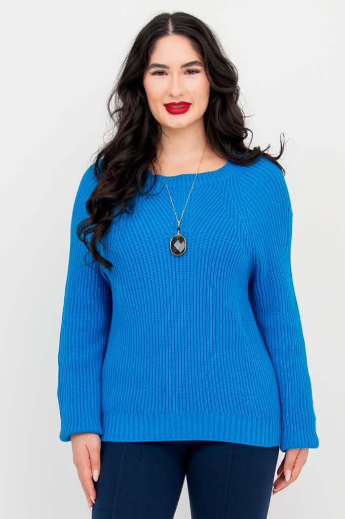 Front view of a model wearing a bright blue knit sweater with a necklace and navy pants