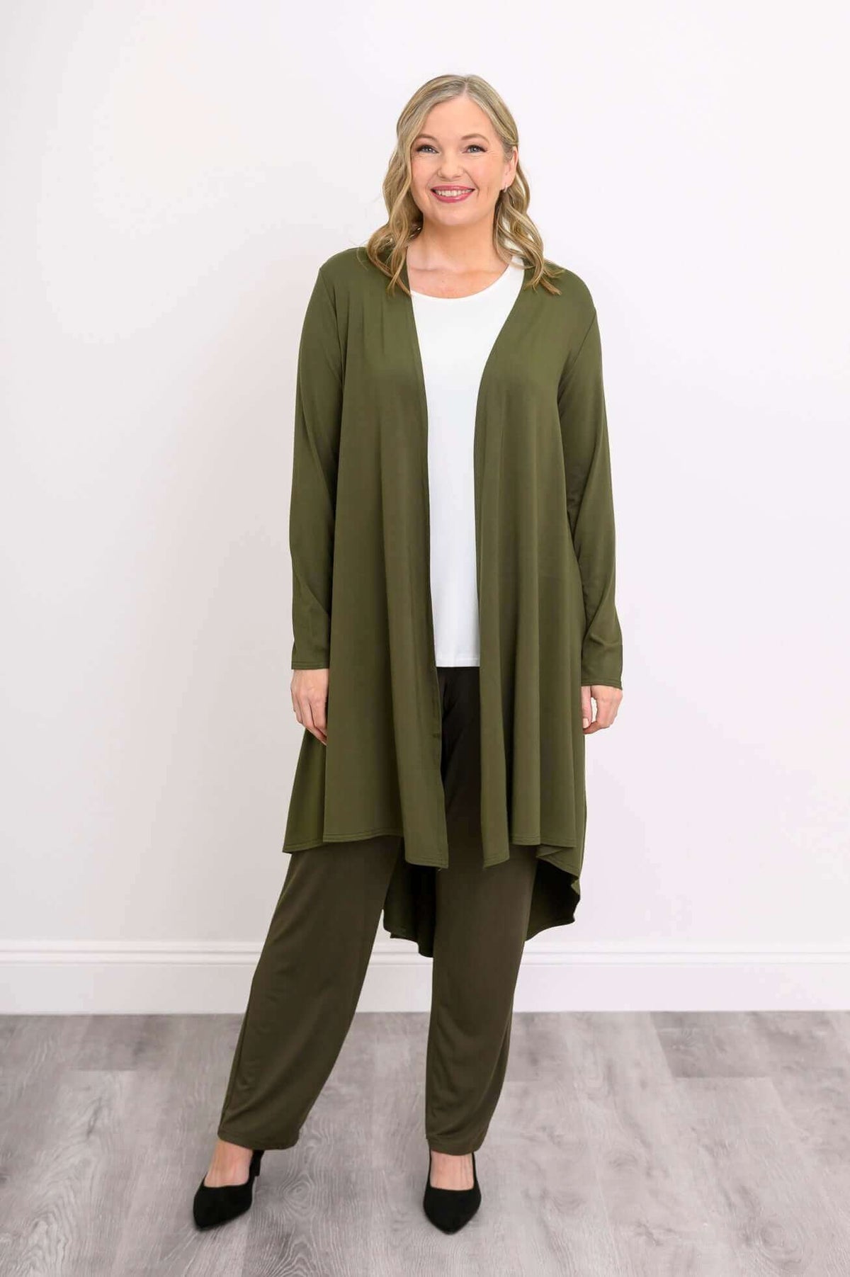 Model smiling in olive green long duster and pants, shown from the front
