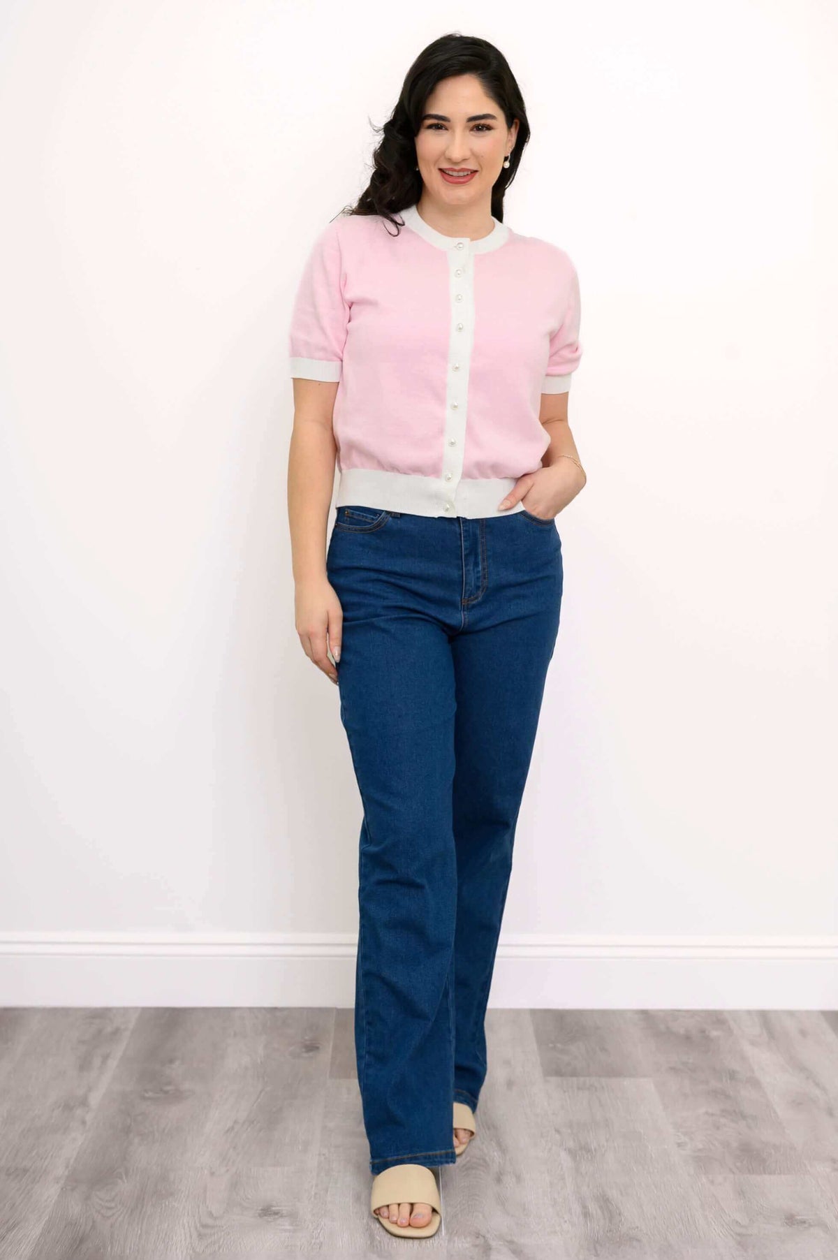 Full front view of model in pink two-tone sweater with faux pearl buttons and blue jeans