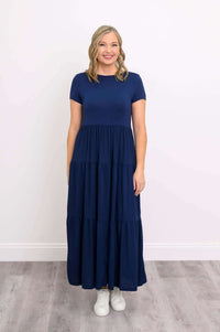 Woman in a navy blue maxi dress with short sleeves, smiling and facing forward