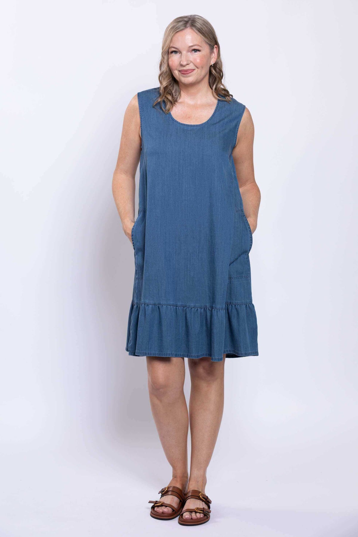 Front view of model wearing sleeveless blue dress with ruffle hem and pockets