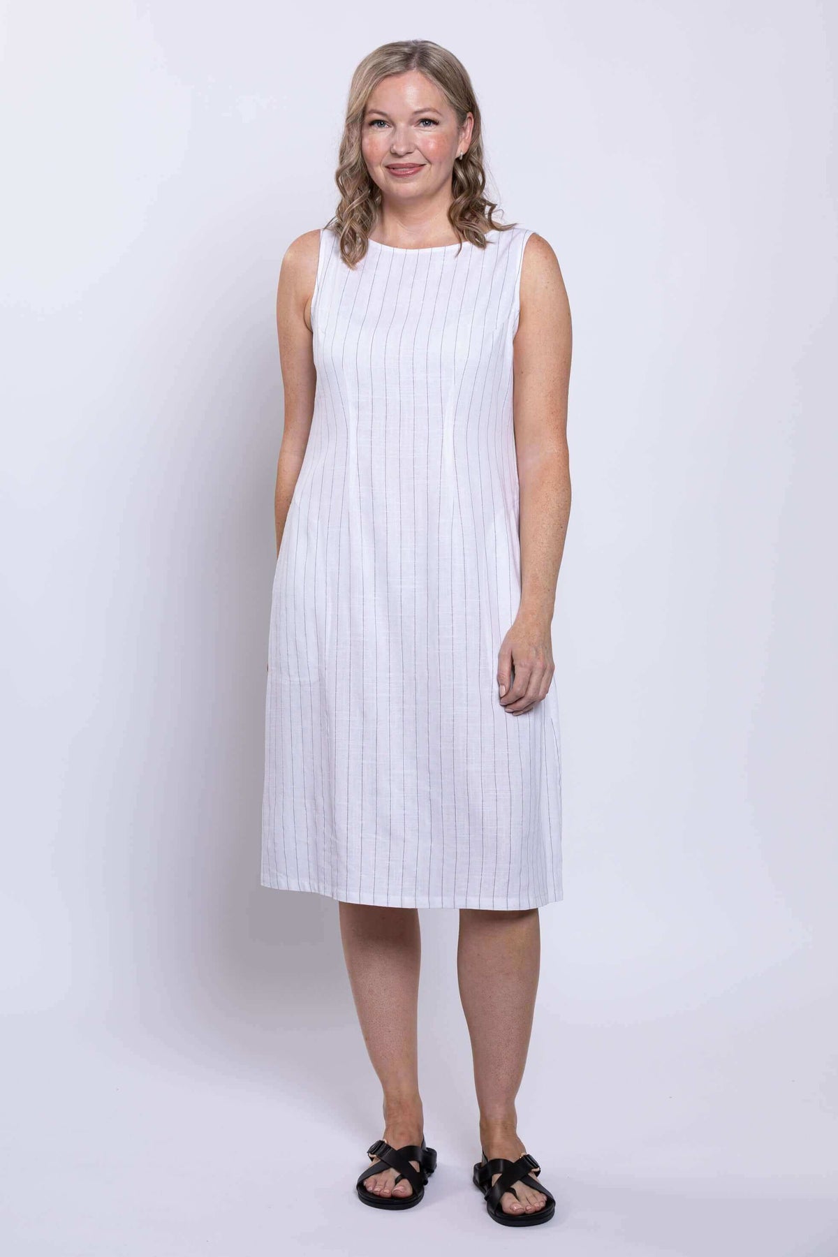 Front view of woman wearing a sleeveless white dress with thin vertical stripes