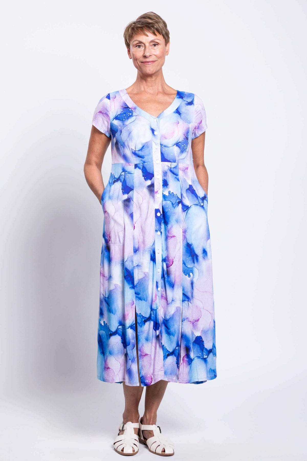 Front view of a woman wearing a watercolor print dress with pockets and white sandals