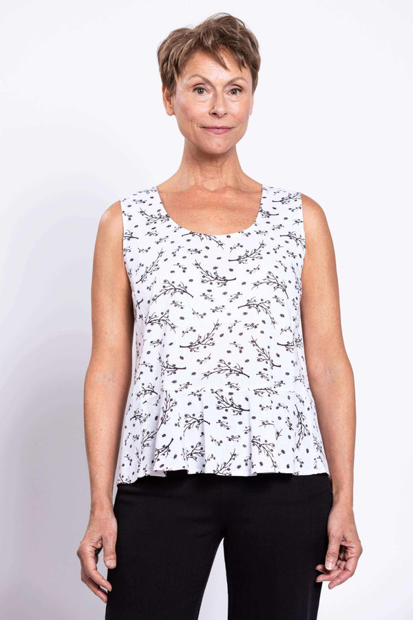 Woman wearing white peplum tank top with black floral pattern, front view