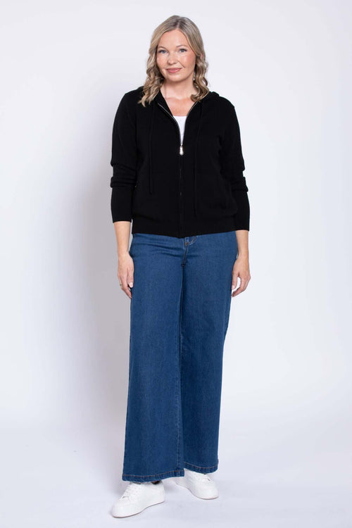 Front view of model wearing wide-leg blue denim jeans, black zip-up hoodie, and white sneakers