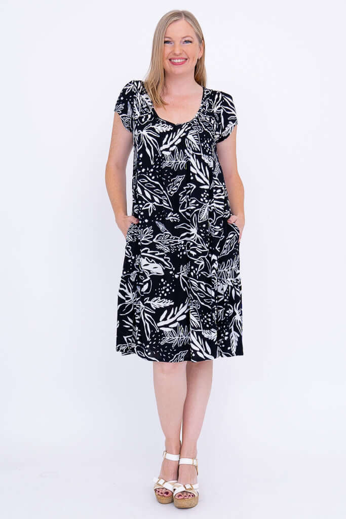 Woman wearing a black and white flowy dress with leafy print, front view