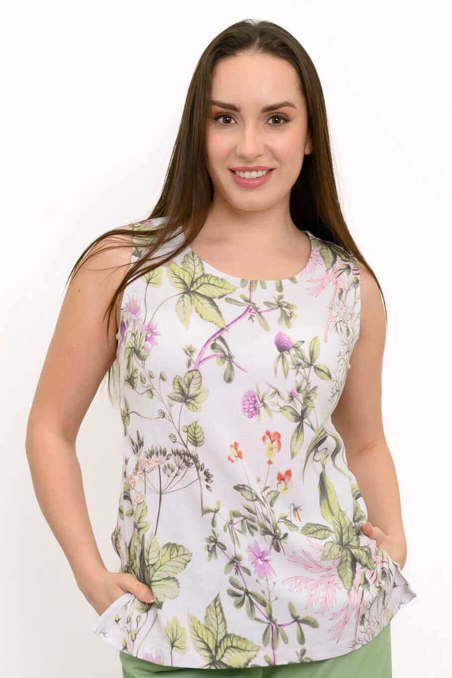Woman wearing a sleeveless white tank with botanical print, green pants, facing forward