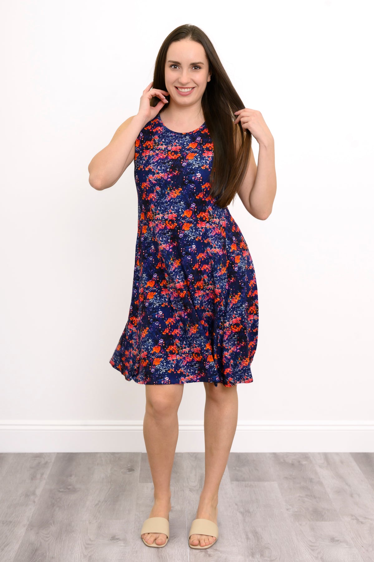 Front view of woman in navy floral sleeveless dress with round neck, posing with hands near hair