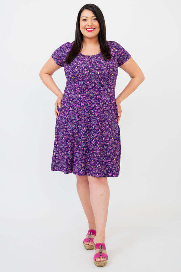 Woman wearing a purple floral bamboo dress with short sleeves, front view, hands on hips