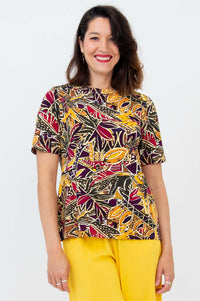 Woman wearing a colorful botanical print short sleeve tee with yellow pants, front view