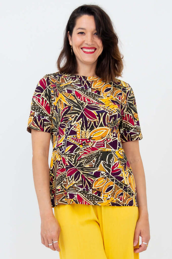 Woman wearing a colorful botanical print short sleeve tee with yellow pants, front view