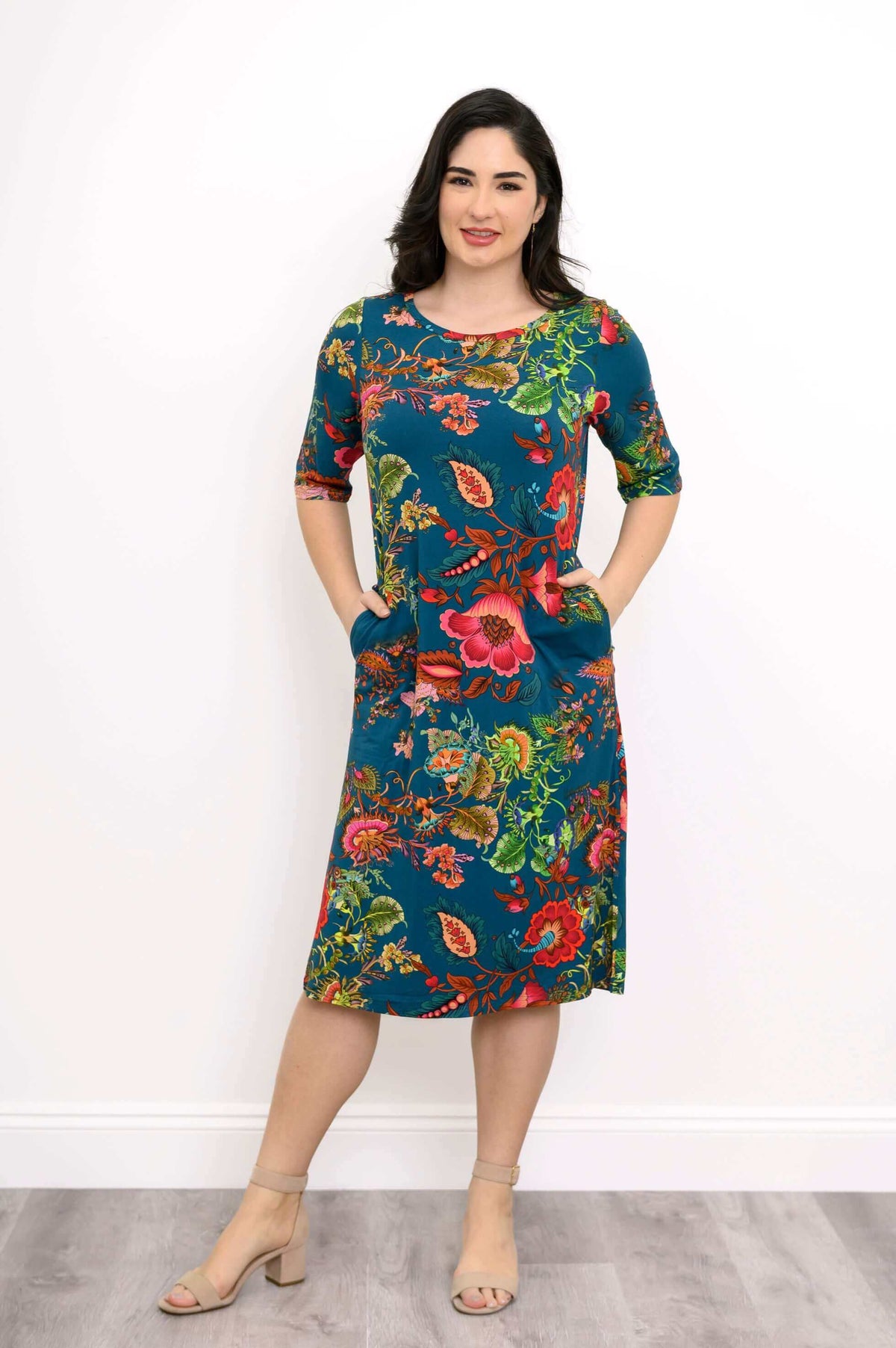 Woman in a vibrant floral bamboo dress with short sleeves and hands in pockets, front view
