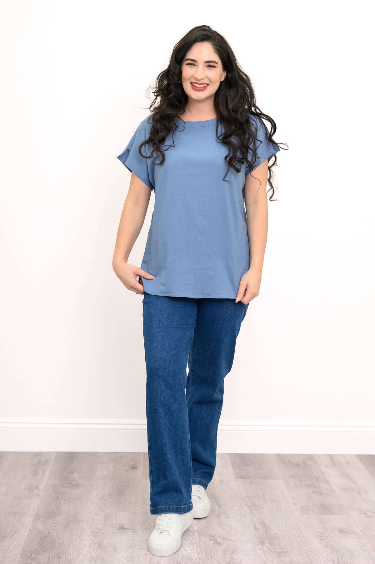 Front view of woman smiling in a blue dolman cap sleeve tee