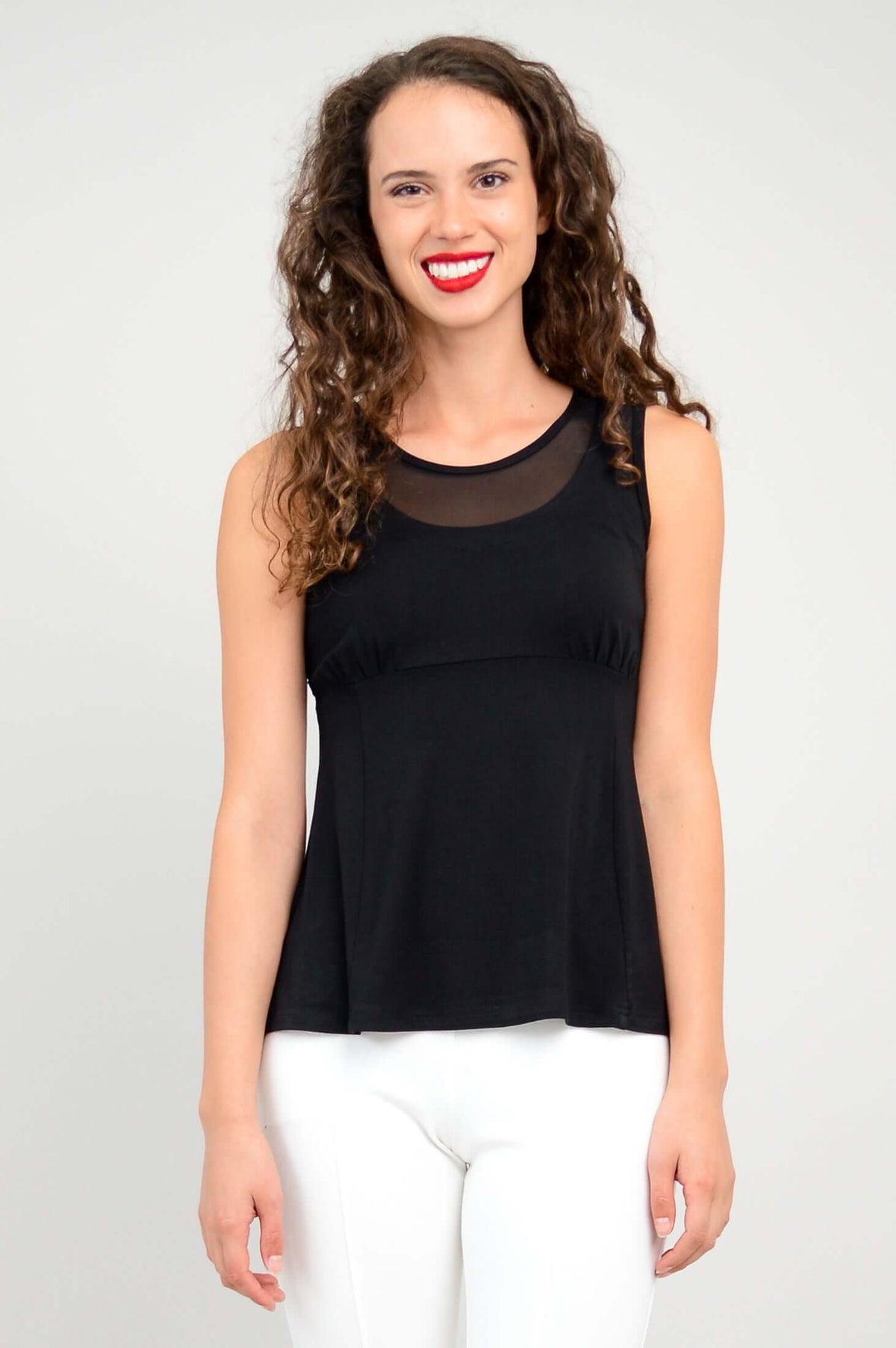 Front view of woman wearing a black tank top with mesh panel and white pants