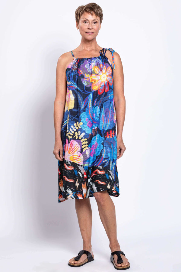 Front view of a woman wearing a sleeveless beach dress with bold colorful floral print and tie shoulder