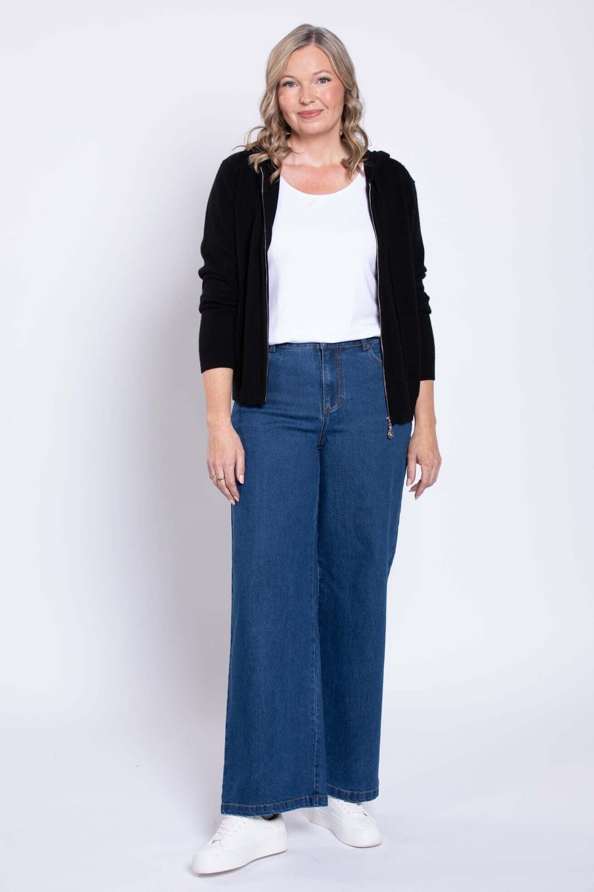Front view of wide-leg blue denim jeans styled with a white top and black hoodie