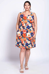 Woman in a colorful floral sleeveless dress with hands in side pockets, facing forward