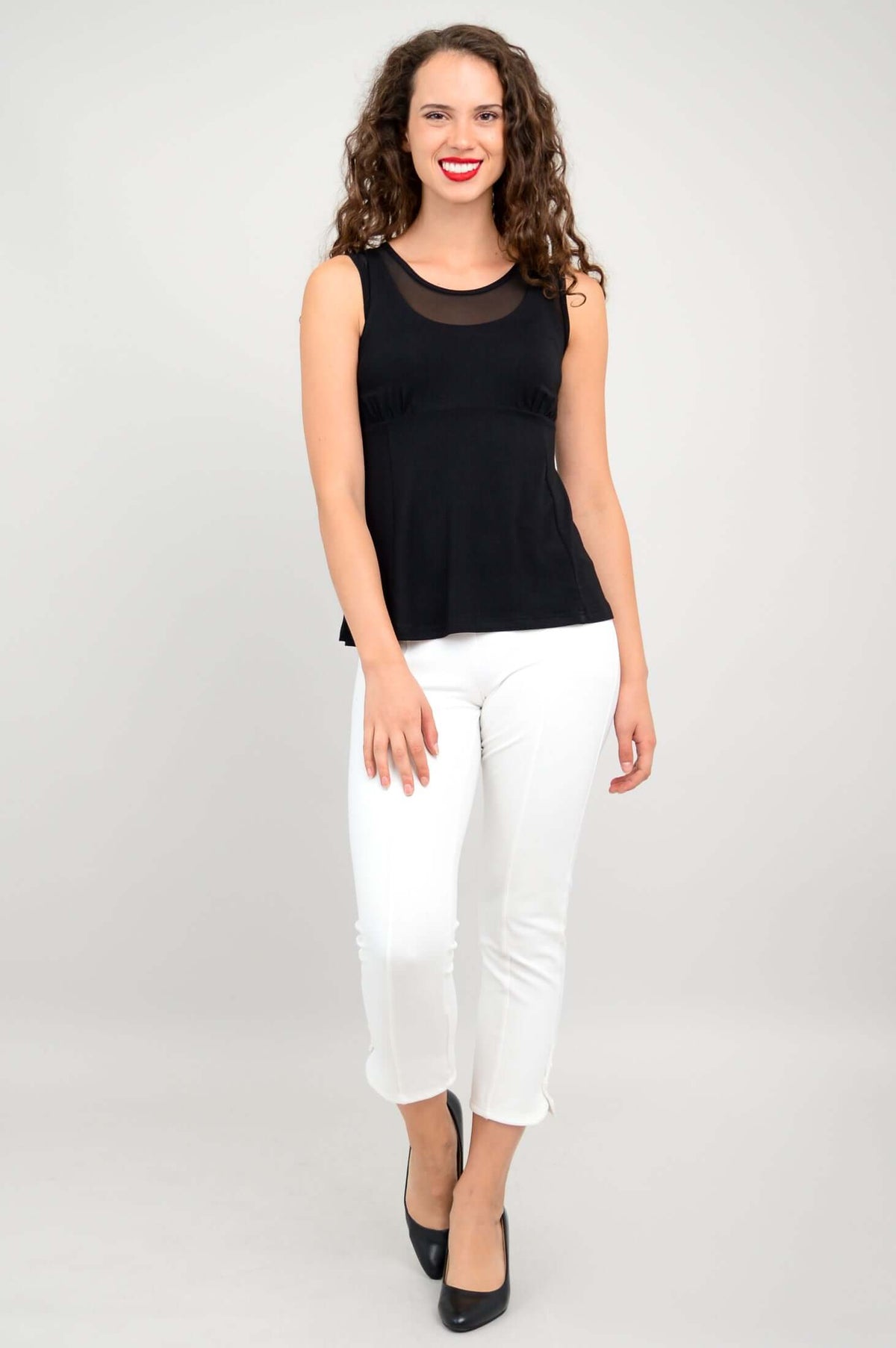 Full-body front view of woman in black mesh tank top and white ankle pants