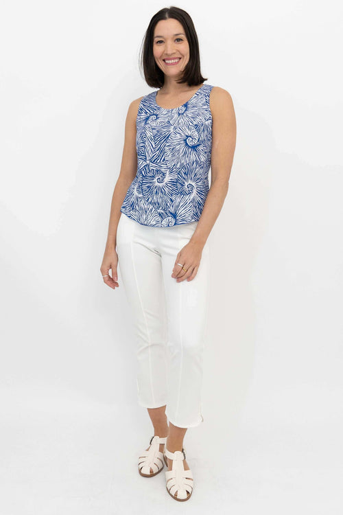 Full-body view of woman in blue and white shell print tank top and white pants