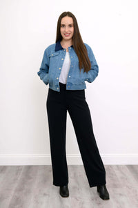 Full-body view of a woman in blue jean jacket and black pants standing on wood floor