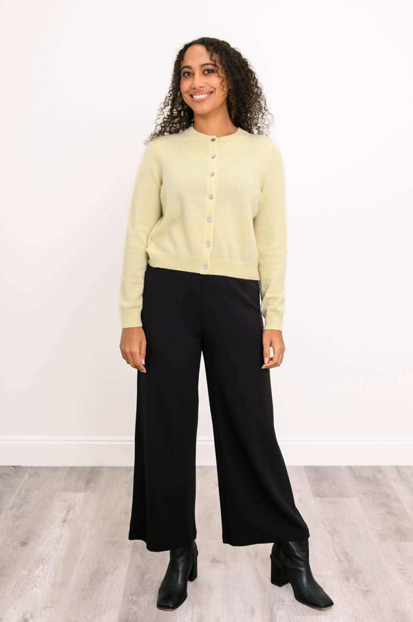 Full-body view of a woman in a light yellow buttoned cardigan and black wide-leg pants