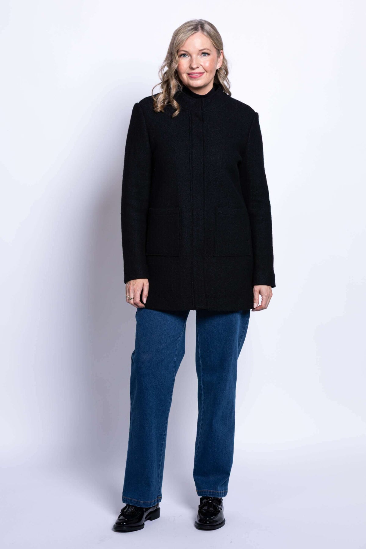 Full-length front view of woman in black boiled wool coat and blue jeans