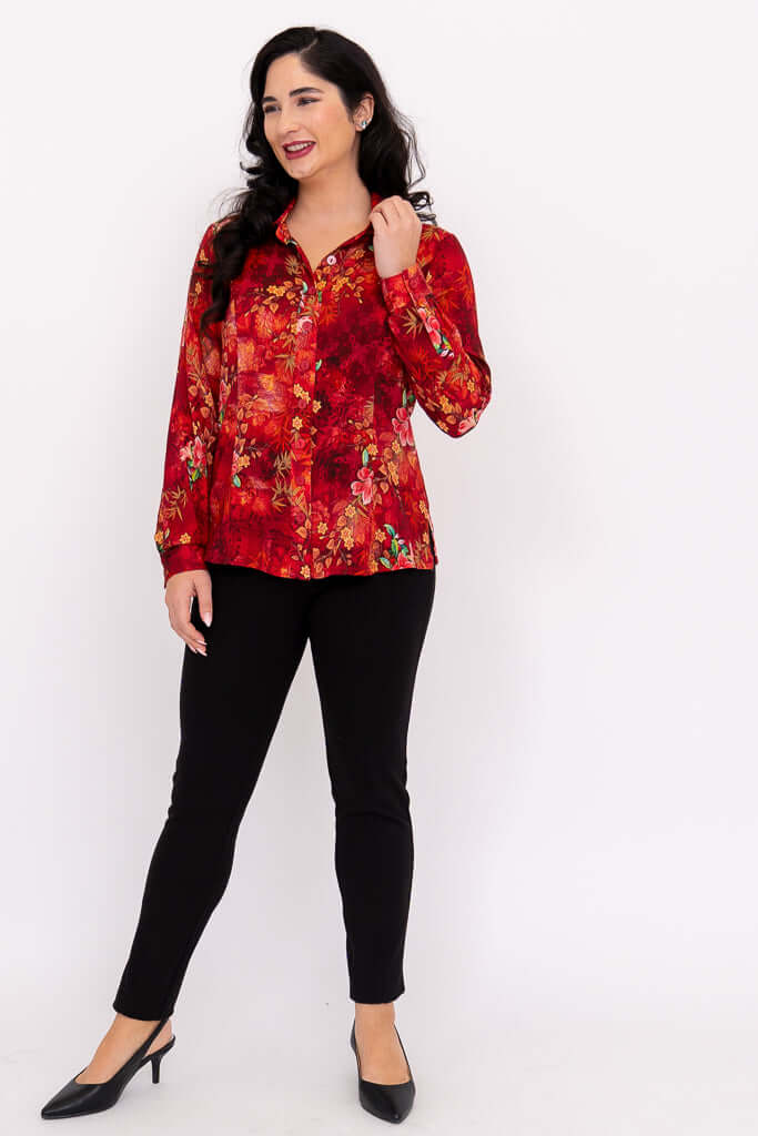 Woman in red floral blouse and black pants, smiling and touching her hair, full-length front view