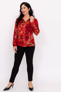 Woman in red floral blouse and black pants, smiling and touching her hair, full-length front view