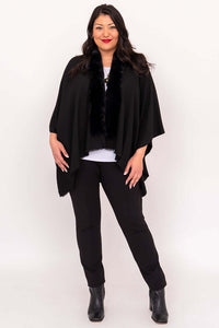 Full-body view of woman in black wrap, white top, black pants, and ankle boots