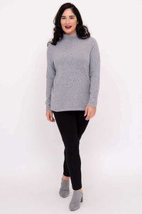 Casual front full-length shot of a woman in a grey mock neck sweater and black pants