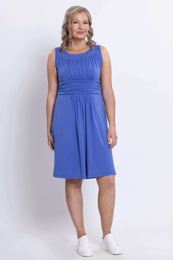 Woman standing in blue dress with fitted waist and pockets, front full-length