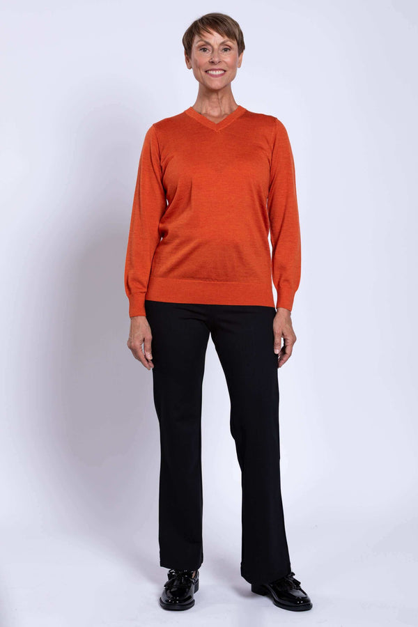 Full-length view of woman in orange V-neck merino wool sweater and black pants