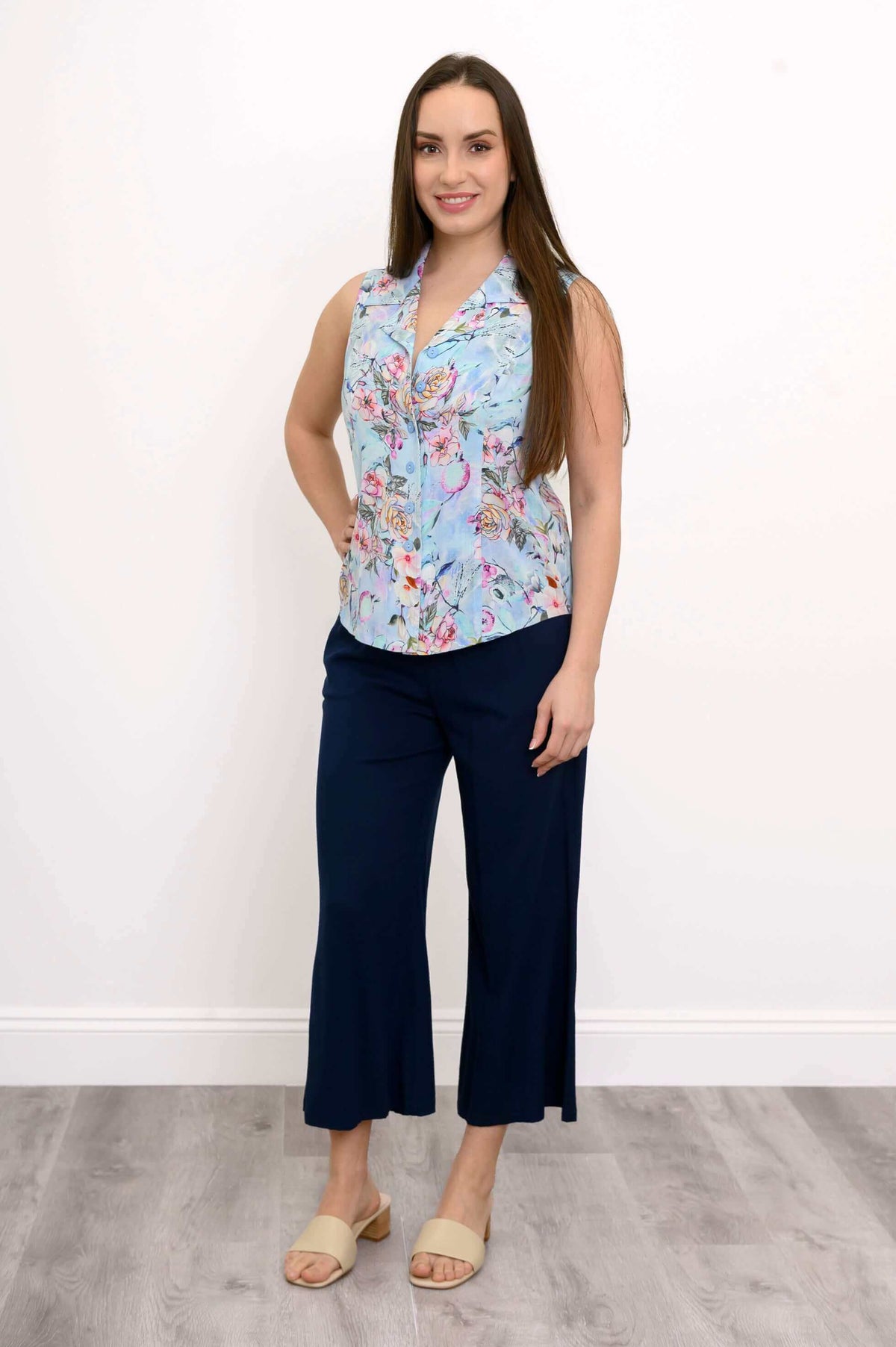 Full body front view of woman in light blue floral sleeveless top and navy pants