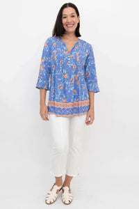 Full body front view of a woman in a blue floral blouse and white pants