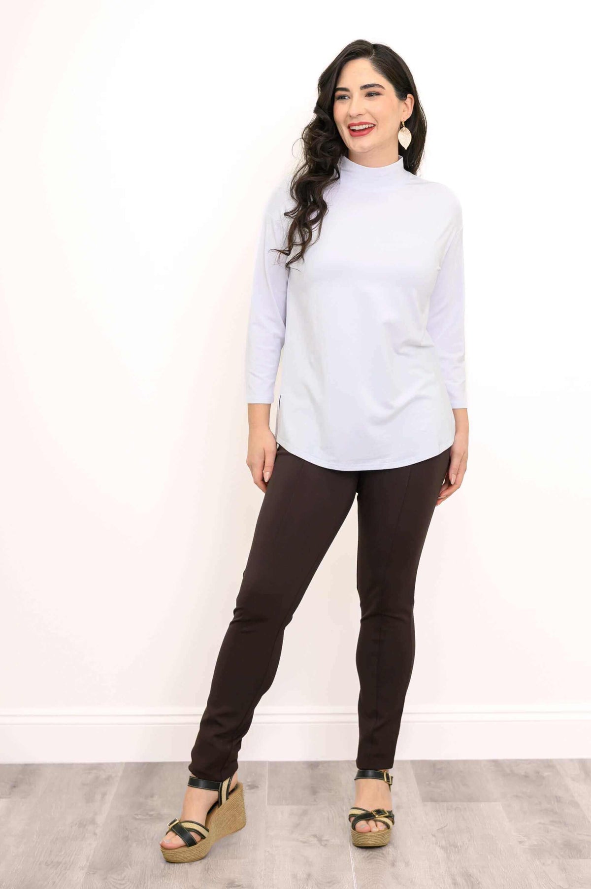 Full body front view of a woman in a white mock neck top and dark pants