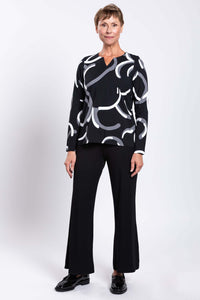 Full body view of woman in black and white abstract print long sleeve top and black pants